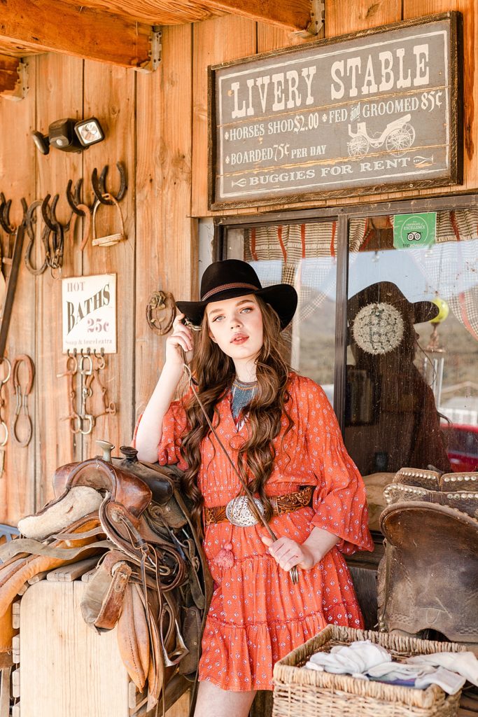Karina poses with a riding crop on the 1870s style front porch during a rustic Sonoran ranch session.