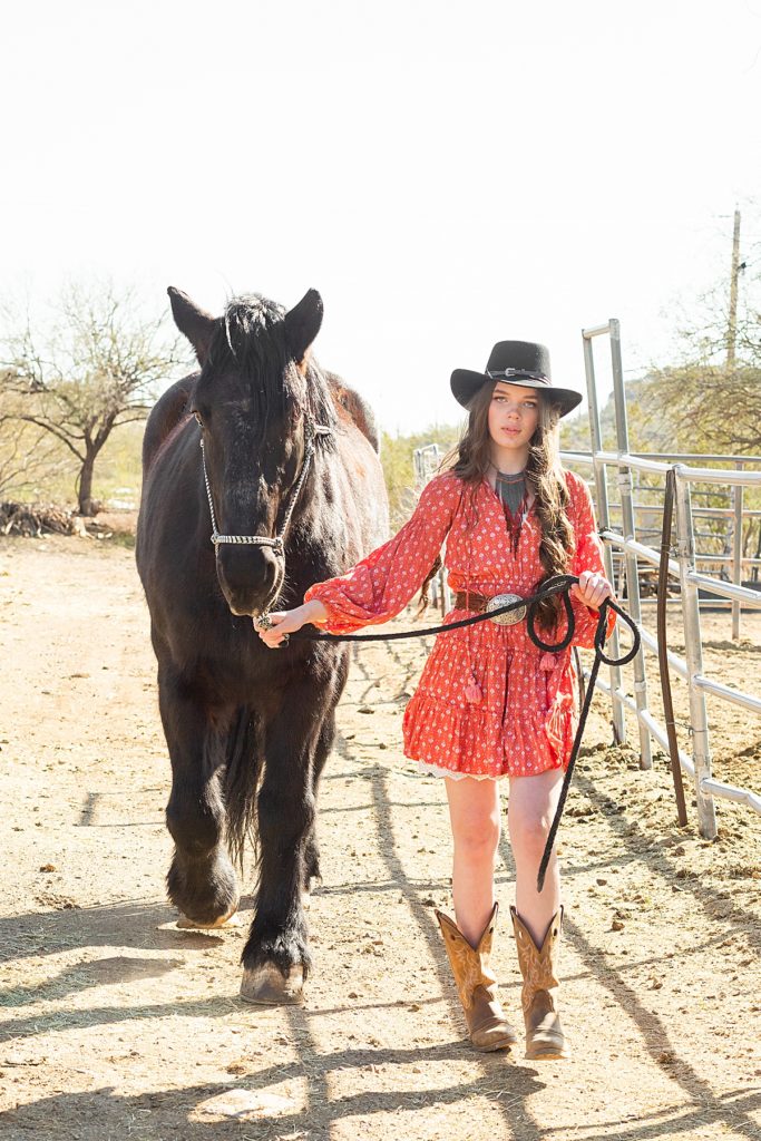 Model Karina leads a stunning black steed down the ranch walkway during a rustic Sonoran ranch styled session.