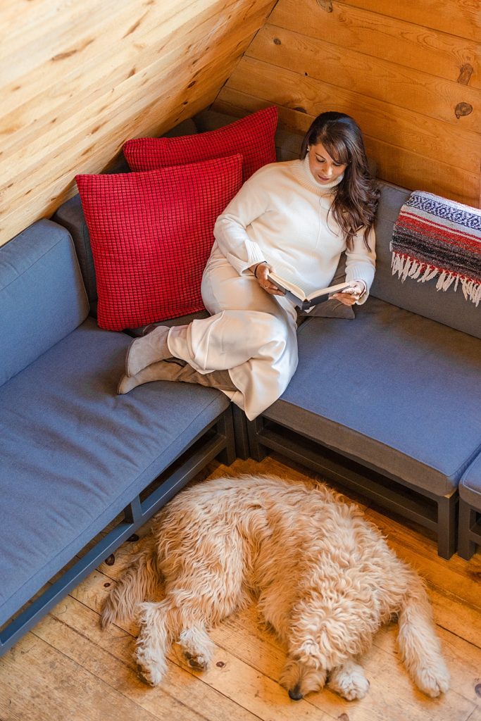 Portrait model Yasmin and Goldendoodle Zayn enjoy a quiet moment reading during an A-Frame cabin portrait session in Flagstaff, Arizona.