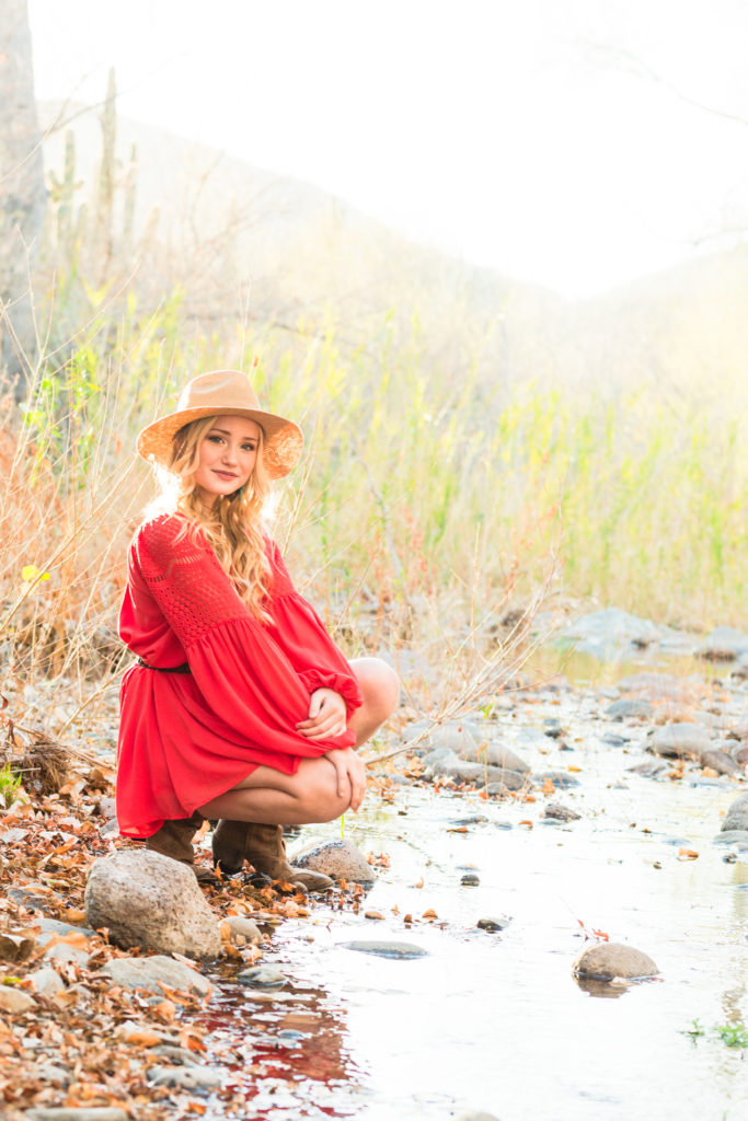 Adorable Addisyn kneels by the silver-streamed creek during a Cave Creek senior portrait session.