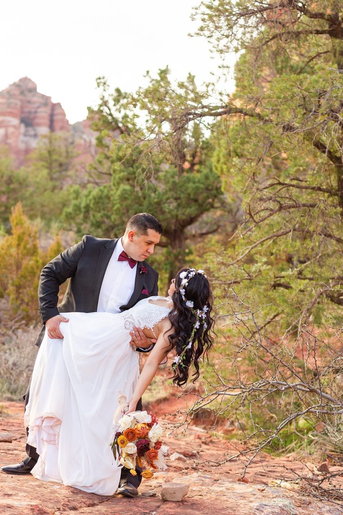 Husband smiles lovingly at wife as he dips her while dancing amidst the red rocks in stunning Sedona, Arizona. 