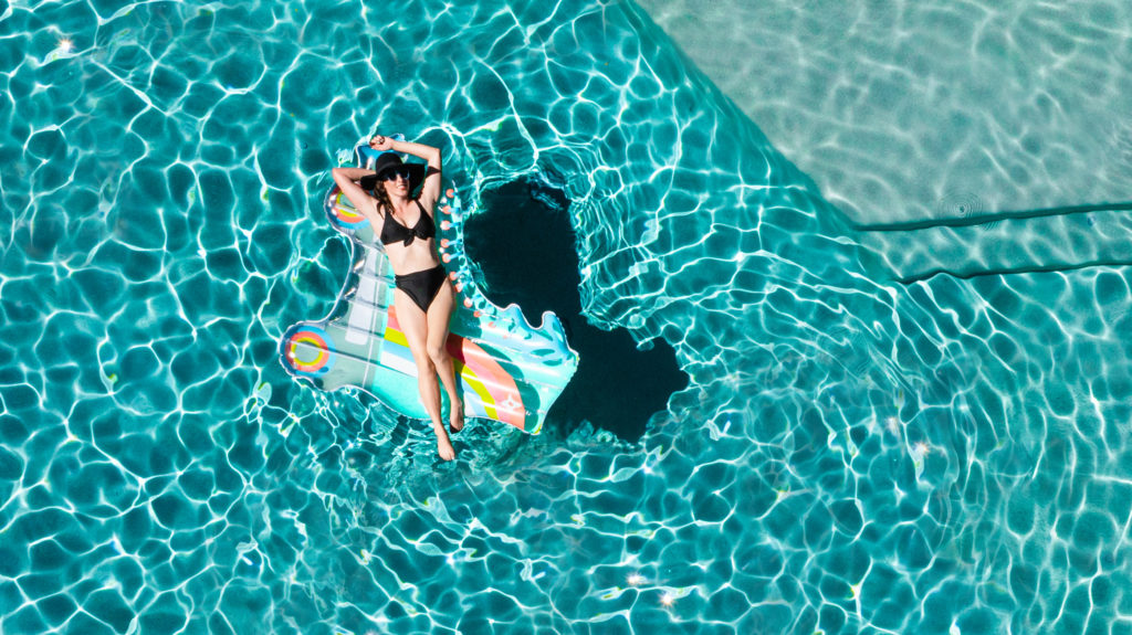 Aerial image of model, Stephanie, floating on a sparkling, aqua-colored pool