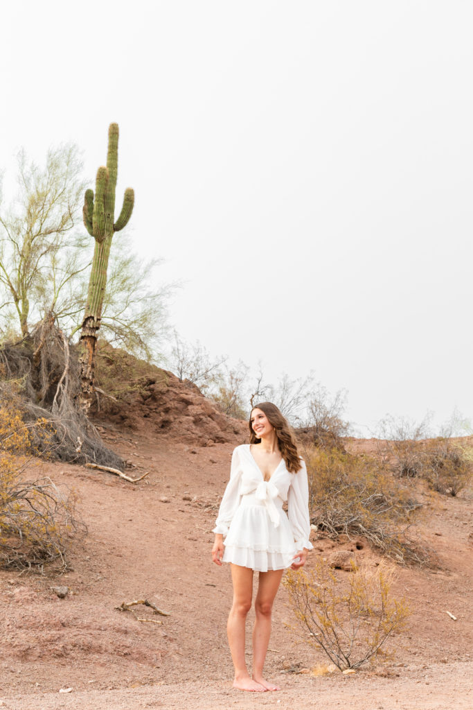 Class of 2022 senior grad Kylie stands amidst red rock and cacti in Papago Park during her portrait session