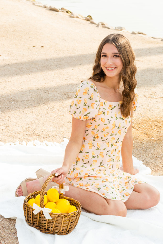 2022 senior grad Kylie grins while wearing a cute yellow dress during her senior portrait session, posing pretty