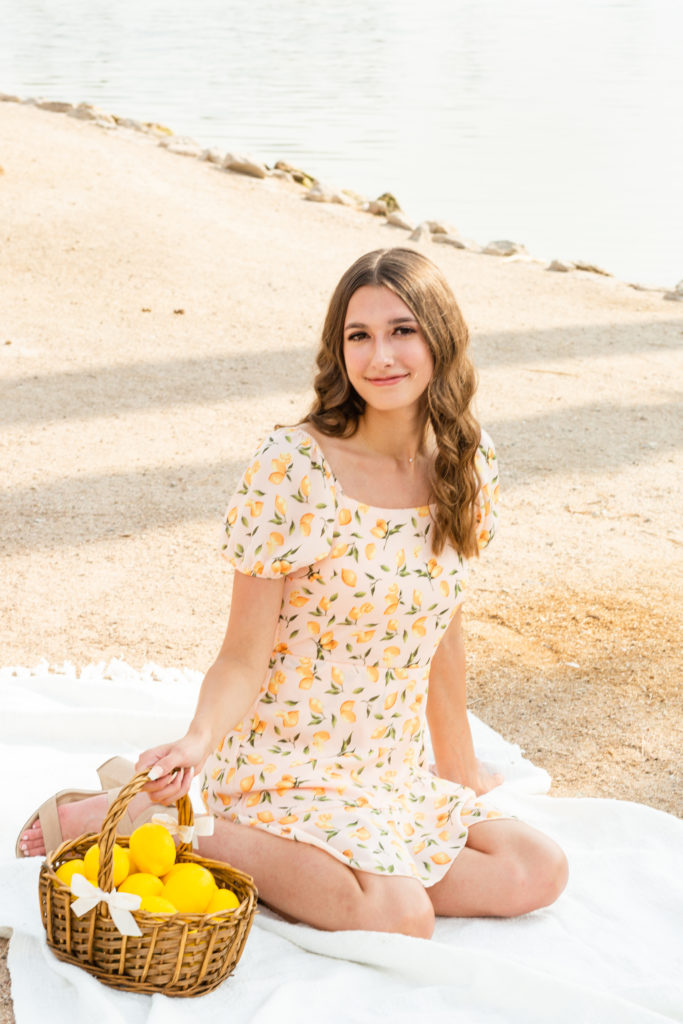 2022 senior grad Kylie smiles as she poses with a prop basket and lemons that match her darling yellow dress during her senior portrait session