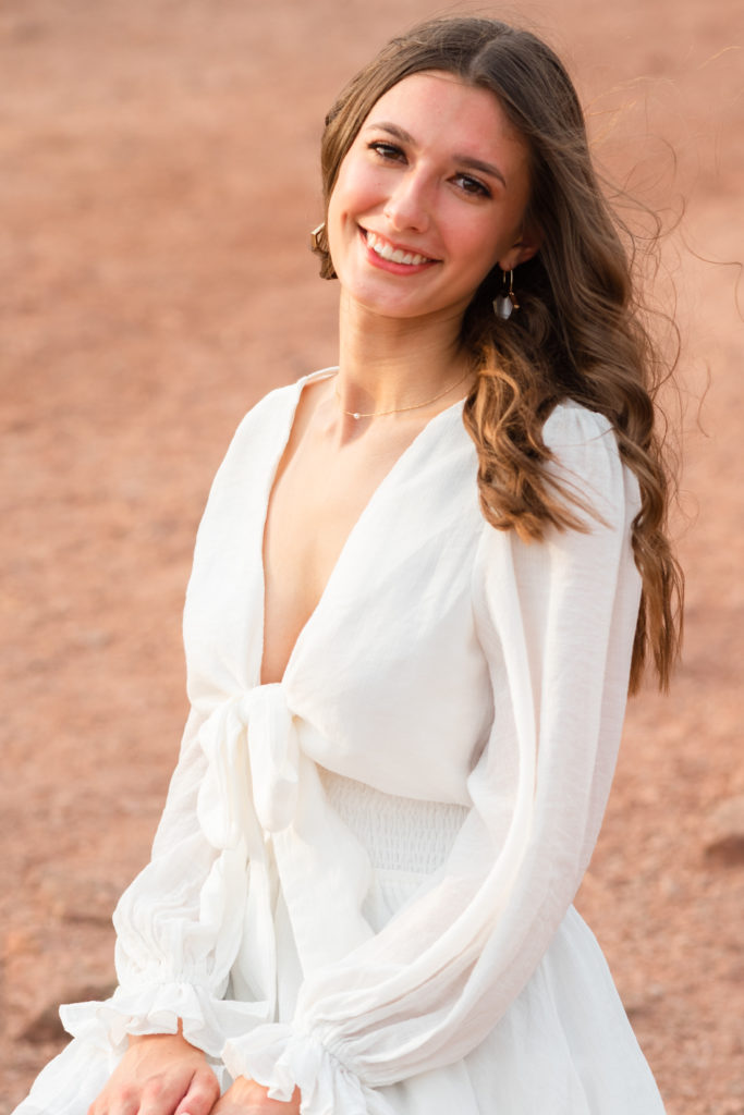 2022 senior grad Kylie, seated on a red rock, smiles during her portrait session