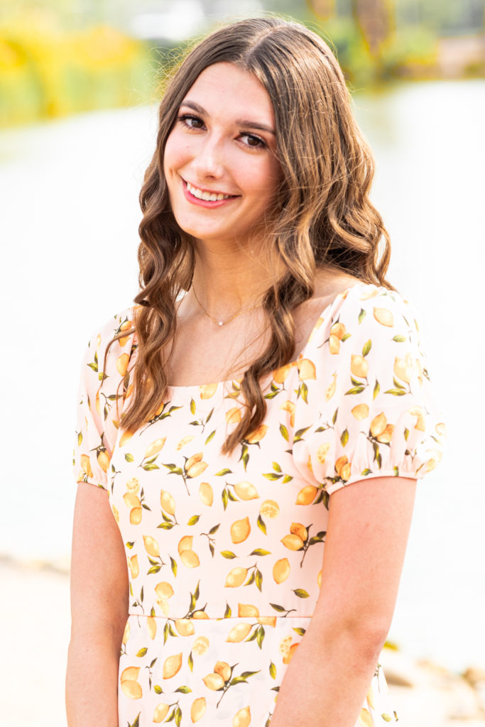 2022 senior grad Kylie smiles in a close-up in a cute yellow dress during her senior portrait session