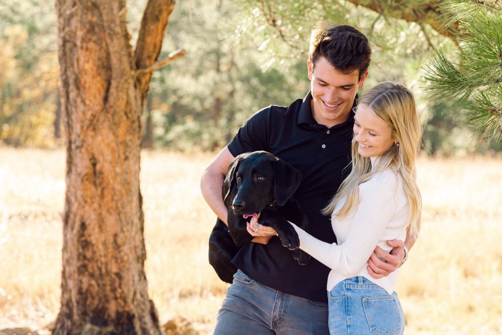 Luke and Kirstin grin as their black lab Corra looks into the distance during a Flagstaff portrait session.