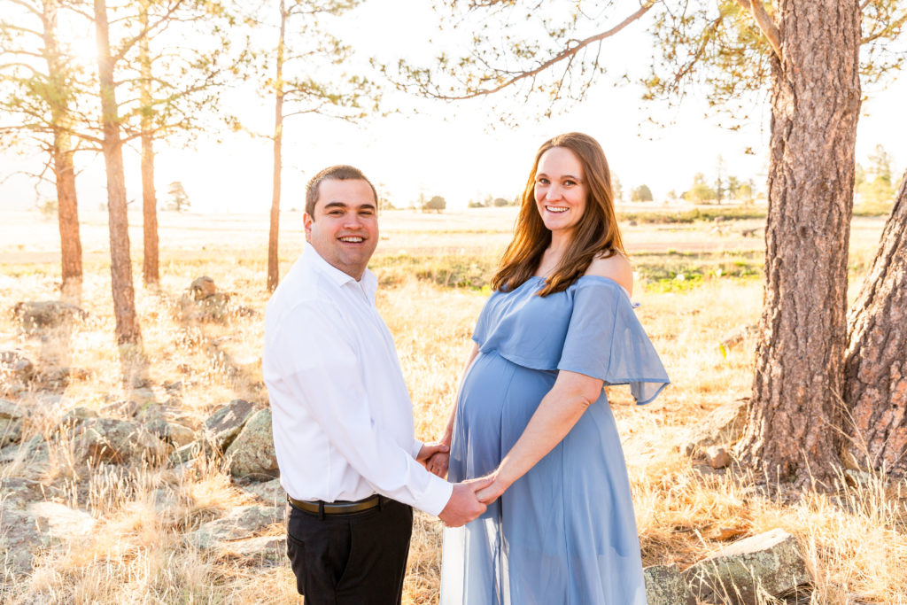 In Flagstaff, Arizona, an expectant mother and father hold hands smiling during a maternity portrait photography session.