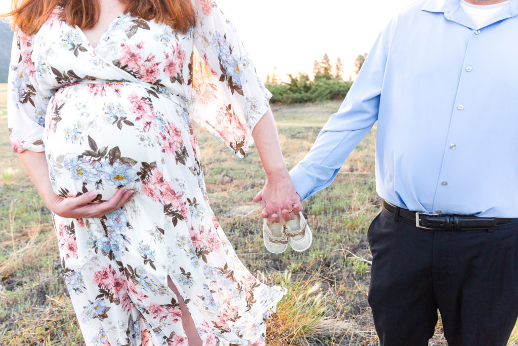 Expecting mother and father hold a small pair of ballet slippers between them for a maternity portrait session in Flagstaff, Arizona