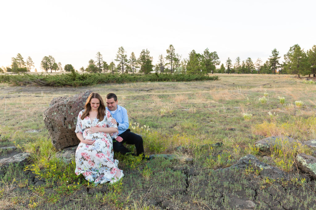 Expectant father and mother smile down at baby while resting in a meadow in Flagstaff, Arizona during a maternity portrait photography session.