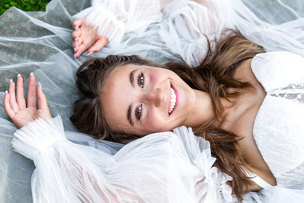 2022 grad Quinn wears a stunning white gown as she lays back with a broad smile during a senior portrait session with Bayley Jordan Photography
