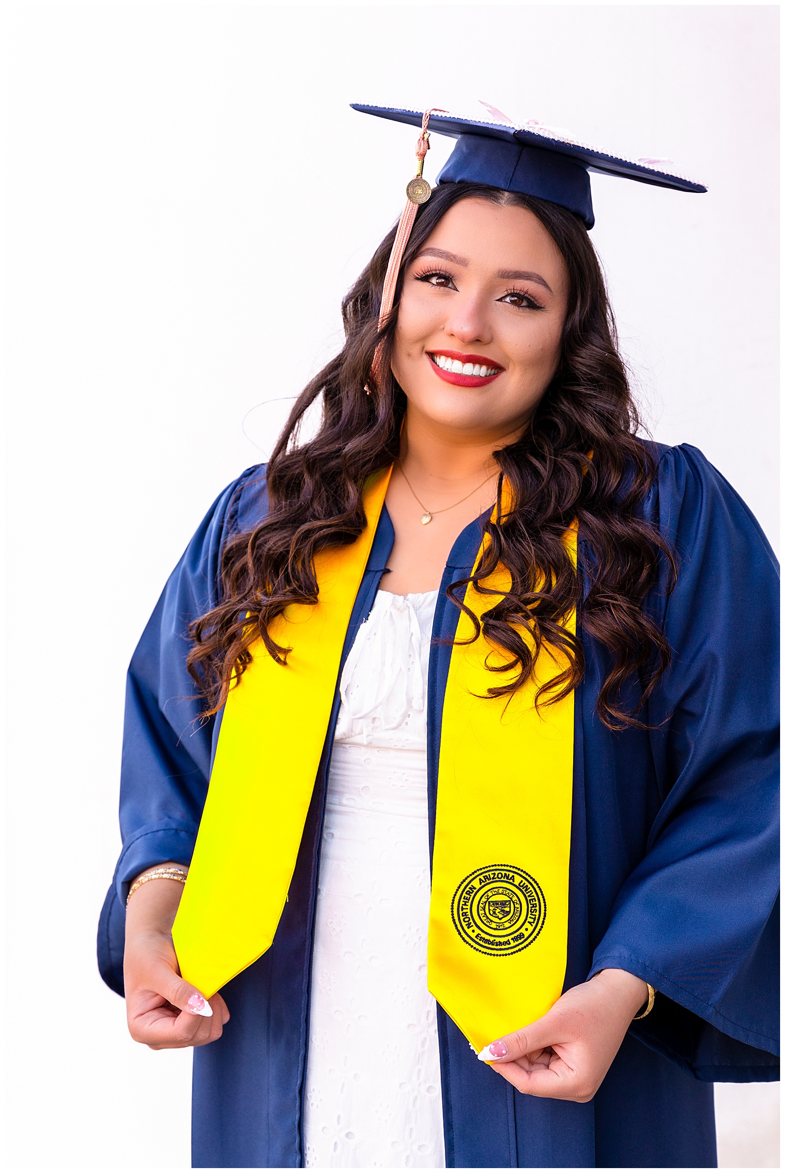 Beautiful graduate from NAU in Flagstaff Arizona shows off her golden sash while wearing navy blue cap and gown.