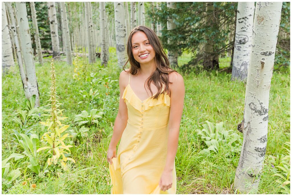 Holly flashes a beaming smile as she walks through a field of wild flowers during her Flagstaff Arizona  graduation portraits with Bayley Jordan Photography