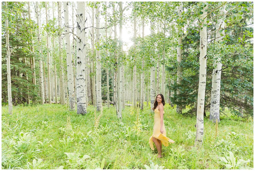 Beautiful Holly dances in a field of flowers surrounded by aspen trees for Flagstaff graduation portraits with Bayley Jordan Photography