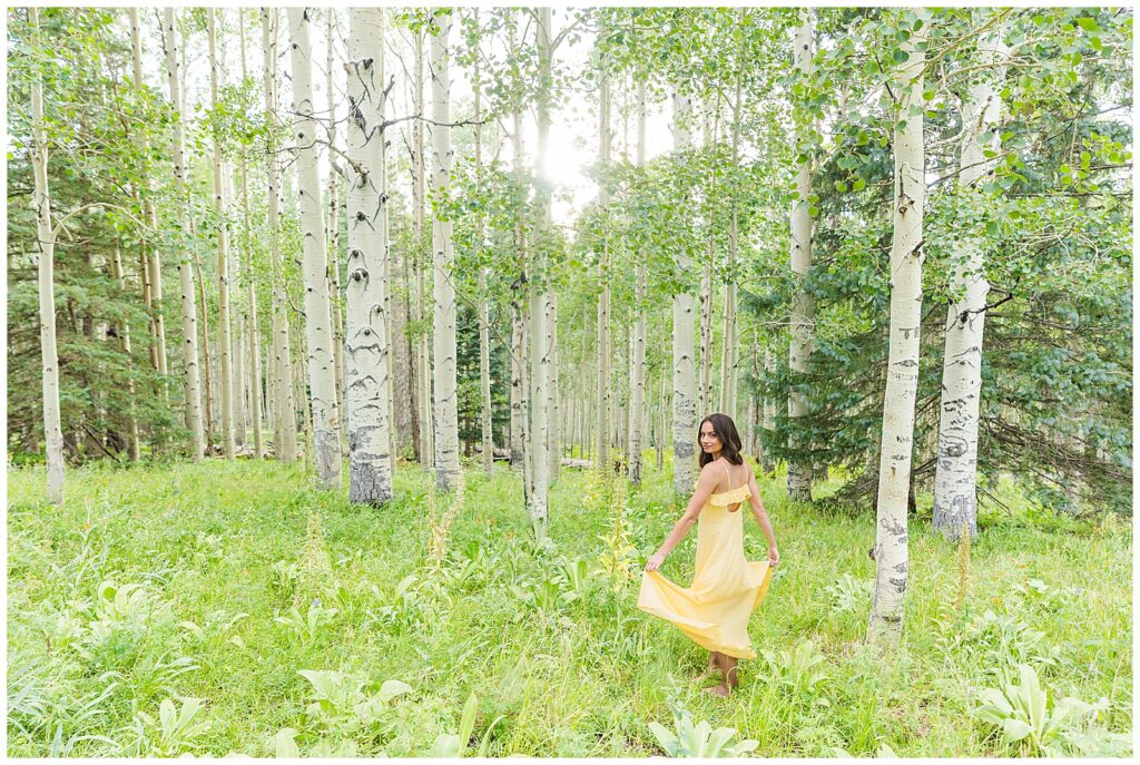 Holly twirls in her long yellow dress in a field of flowers surrounded by aspen trees for Flagstaff graduation portraits with Bayley Jordan Photography