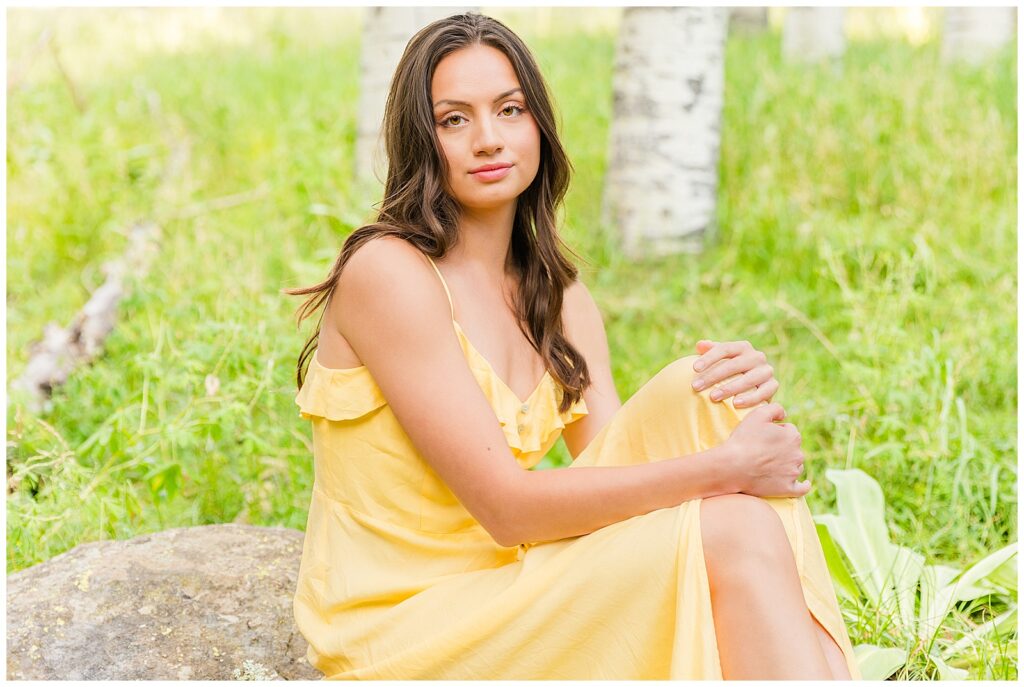 Holly poses upon a rock wearing a bright yellow dress during her editorial NAU graduation portraits in Flagstaff, Arizona with Bayley Jordan Photography
