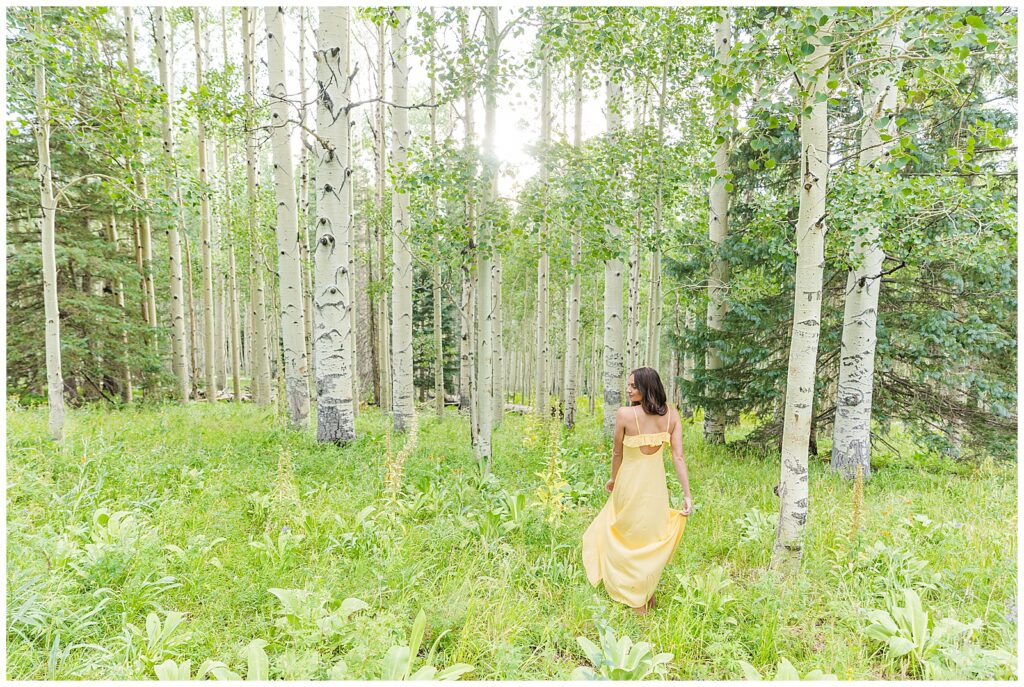 Holly swishes her long yellow dress in a field of flowers surrounded by aspen trees for Flagstaff graduation portraits with Bayley Jordan Photography