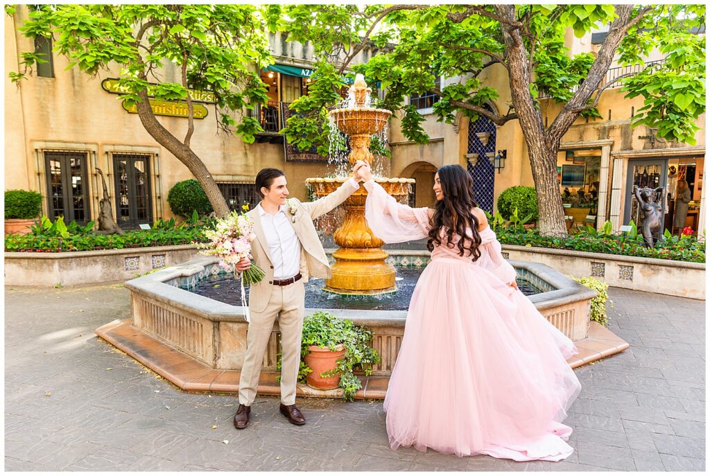 Couple dressed up in flowing pink gown and tan suite, dancing during anniversary portrait session at Tlaquepaque Arts & Shopping Village in Sedona, Arizona.