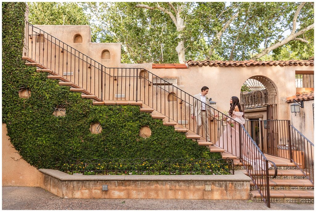 Couple ascends a grand staircase during celebratory portrait session at Tlaquepaque Arts & Shopping Village in Sedona, Arizona at sunset. 